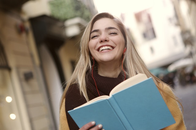 smiling-woman-in-black-and-yellow-long-sleeve-shirt-holding-book